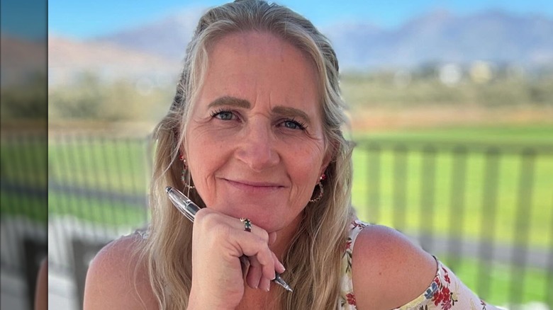 Christine Brown sports a light smile as she holds a pen close to her chin