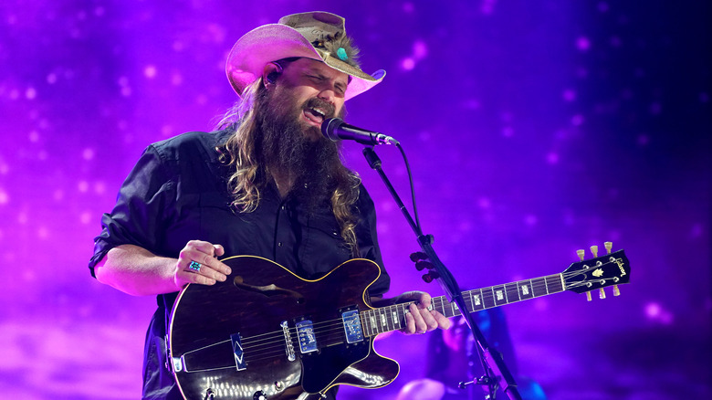 Chris Stapleton, wearing a cowboy hat, playing guitar and singing onstage in 2021