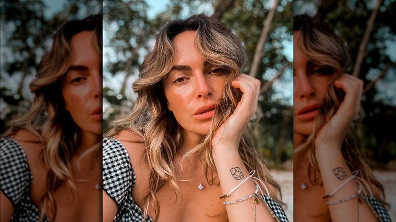 Katie Flood, looking tired, selfie, beachy hair, showing tattoo, on a beach, 2021 photo