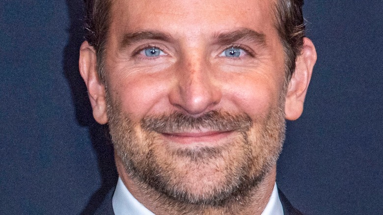 Bradley Cooper smiles in front of blue background