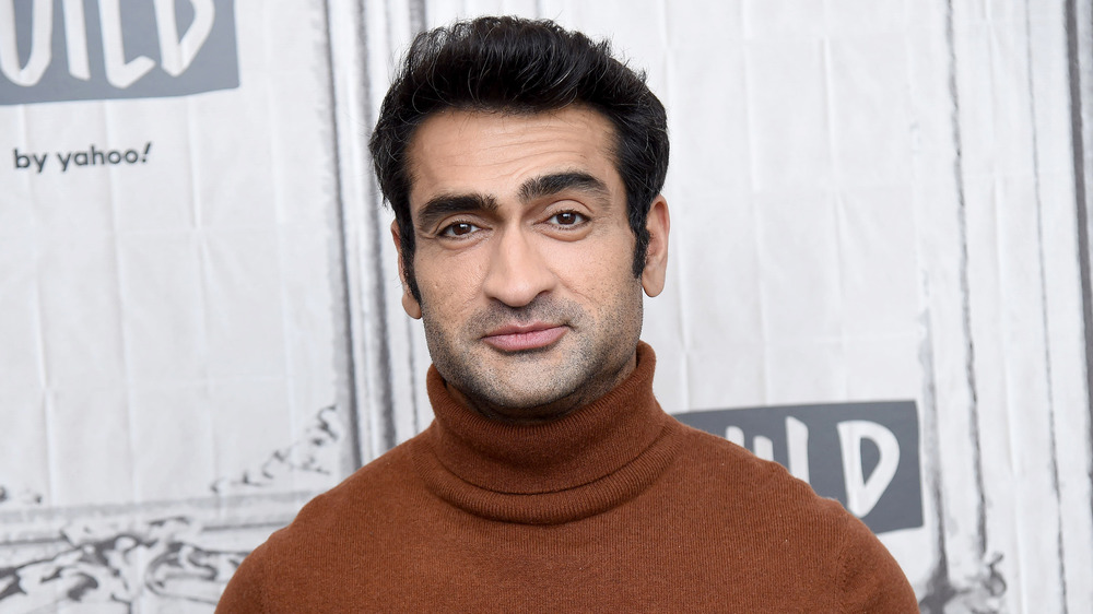 Kumail Nanjiani slightly smiling on the red carpet in a brown turtleneck sweater