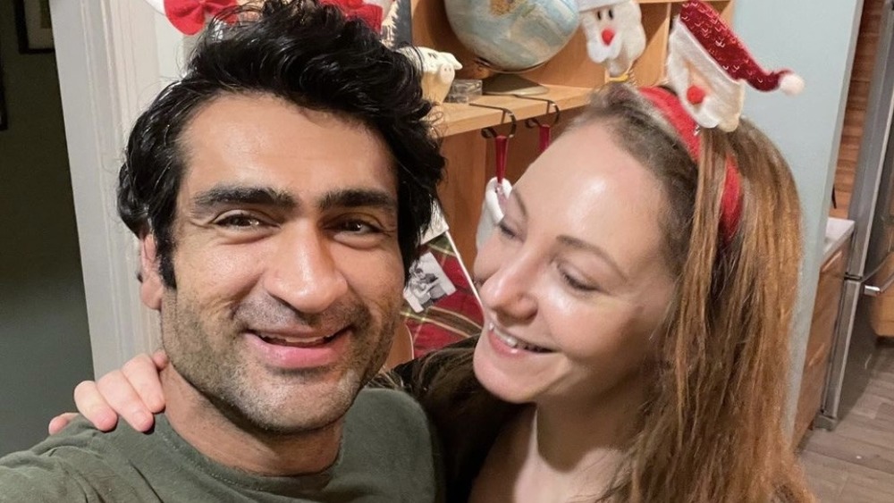 Kumail Nanjiani, selfie, smiling, in Christmas hat; Emily Gordon, smiling, in Christmas hat, looking at husband 