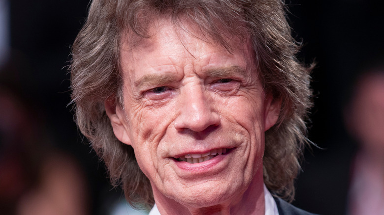 Mick Jagger smiles in a dark suit.