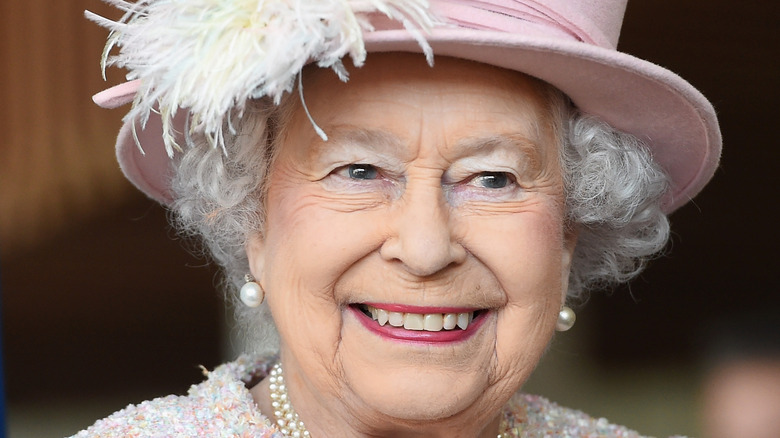 Queen Elizabeth smiling and wearing pink hat