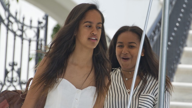 Dressed is a stripped shirt, Sasha Obama makes a face while walking behind Malia Obama.