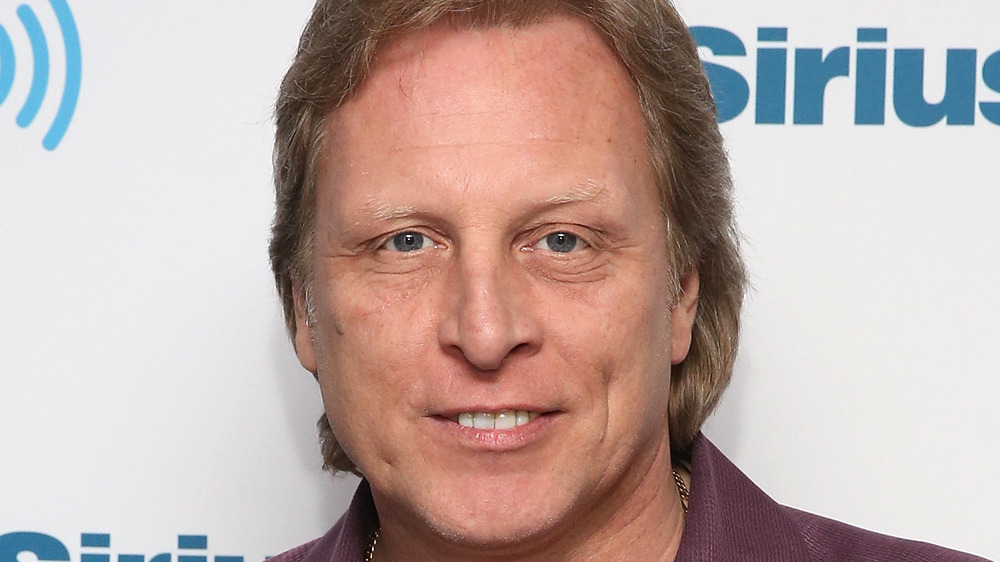 Sig Hansen smiles in front of a photo wall at a radio show