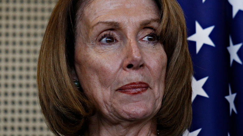 Nancy Pelosi looking to the side in front of American flag