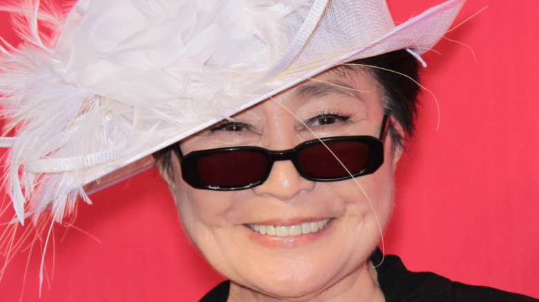 Yoko Ono smiling in sunglasses and a feathered hat