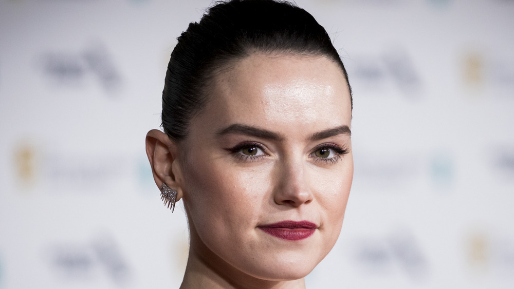 Daisy Ridley wearing red lipstick, spiky earrings and her hair pulled back