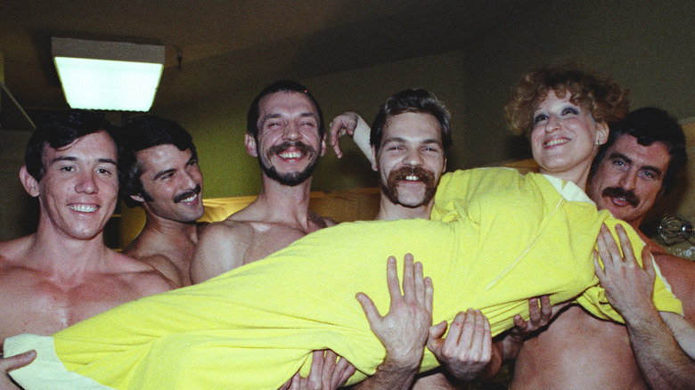 Bette Midler in a yellow dress being carried by a group of men
