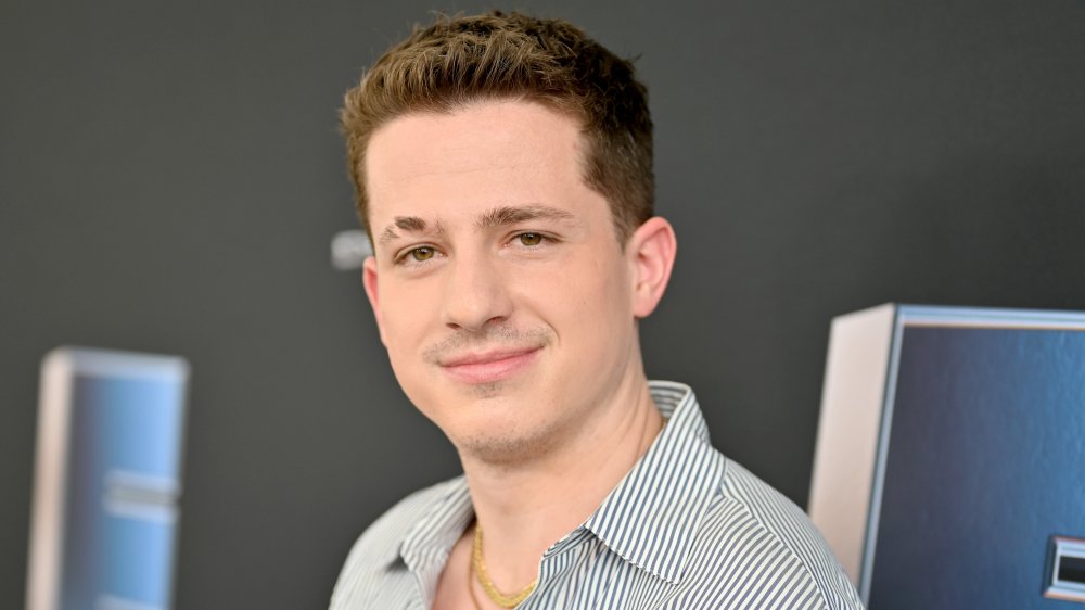 Charlie Puth in a blue-and-white striped button down, grinning at an event