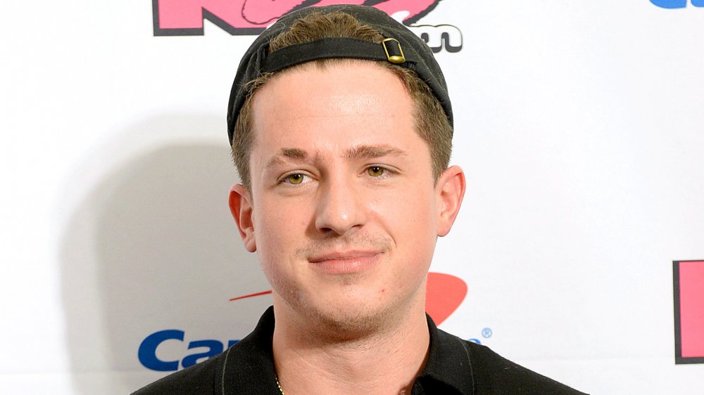 Charlie Puth in a black shirt and backwards hat, posing with a neutral expression at an event