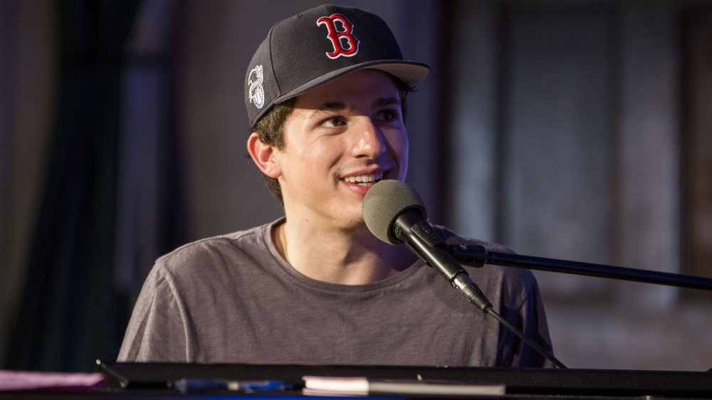 Charlie Puth singing at a piano, wearing a grey t-shirt and Boston Red Socks baseball cap