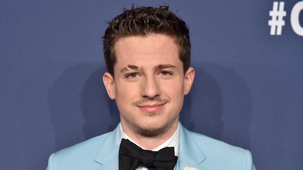 Charlie Puth in a light blue suit with white shirt and black bow tie, grinning while posing on a red carpet