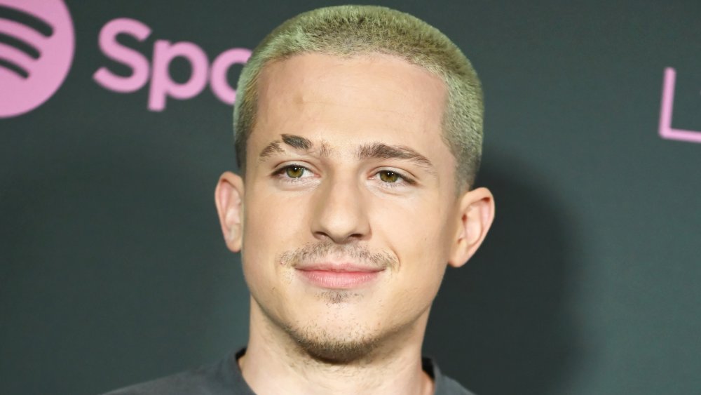 Charlie Puth in a gray shirt with a bleached buzz cut, grinning at a Spotify event
