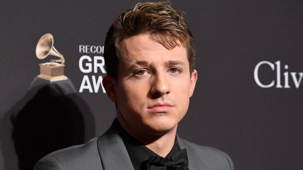 Charlie Puth in gray suit with black shirt and bow tie, looking solemn on the Grammys red carper