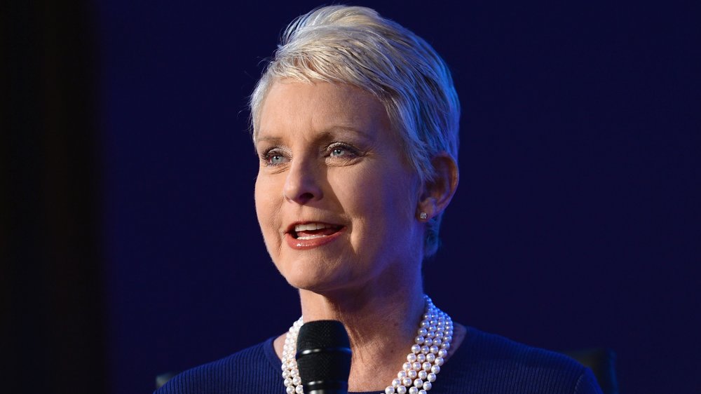 Cindy McCain in a blue dress and pearl necklace, speaking into a mic