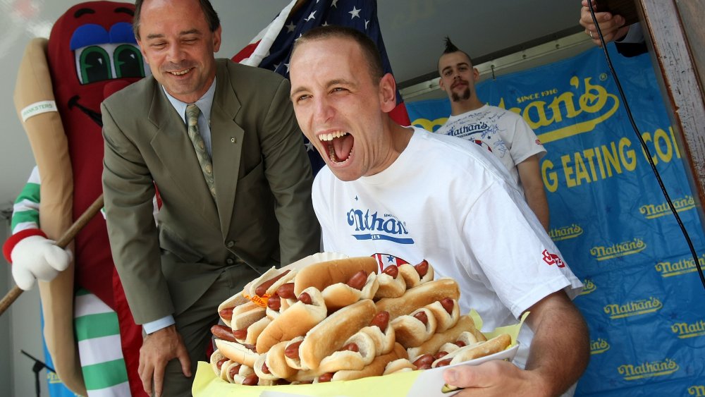 Joey Chestnut laughing while carrying a tray of hot dogs