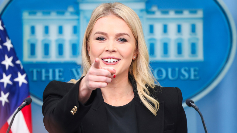 Karoline Leavitt smiling and pointing in the press briefing room of the White House