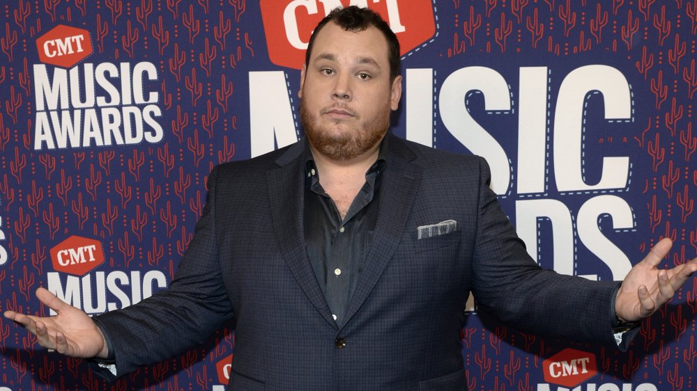 Luke Combs in a gray suit, posing with a shrug at the CMT Music Awards