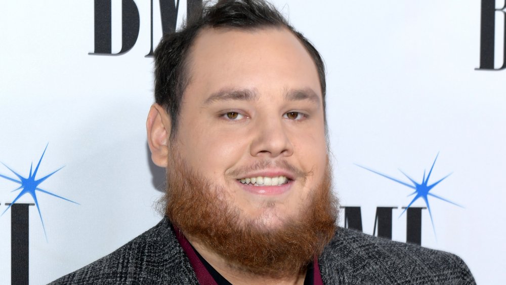 Luke Combs in a grey tweed blazer, smiling at a red carpet event