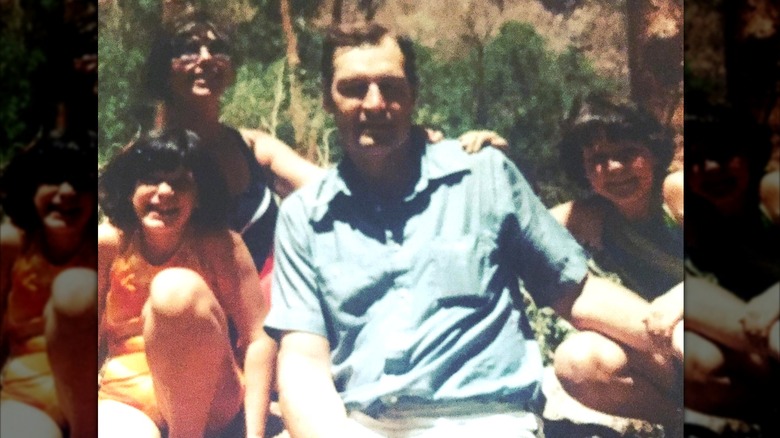 Charles smiling while sitting outside with his family surrounding him