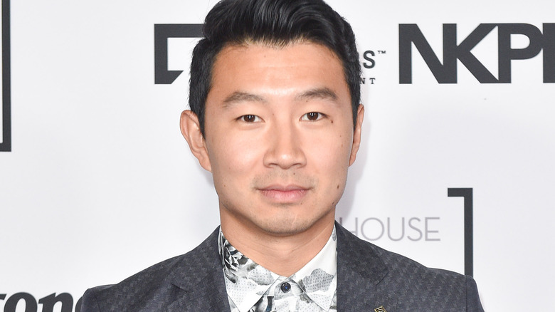 Simu Liu in a grey suit, smiling