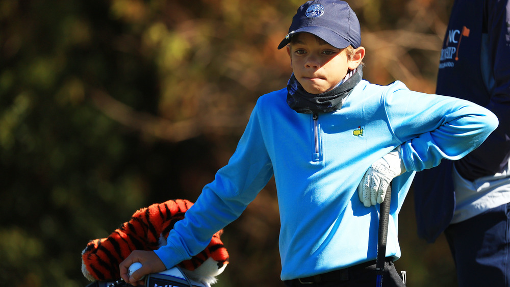 Charlie Woods leaning on a golf club and bag 