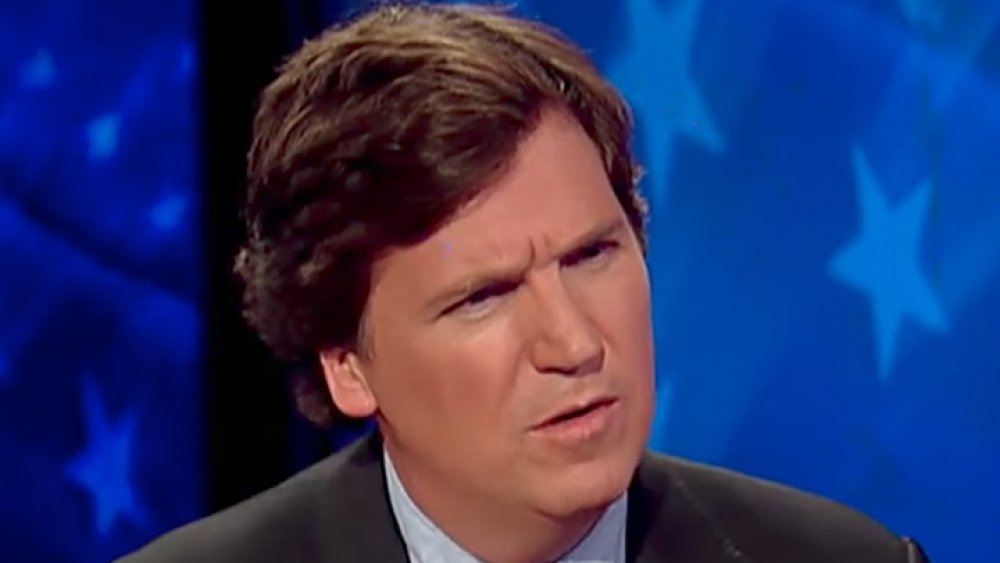 Tucker Carlson in a grey suit, looking confused during an interview on his show