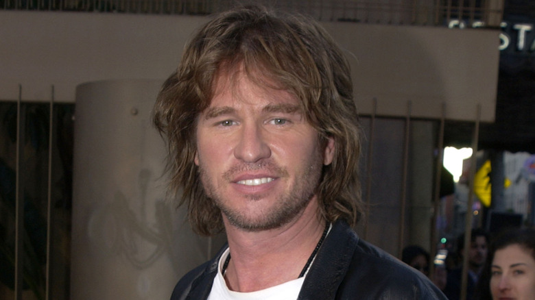 Val Kilmer, smirking while posing at an event