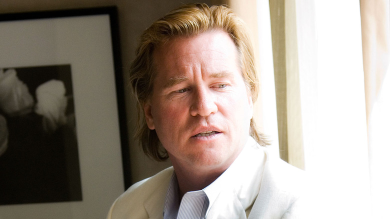 Val Kilmer wearing a white jacket while sitting by a window