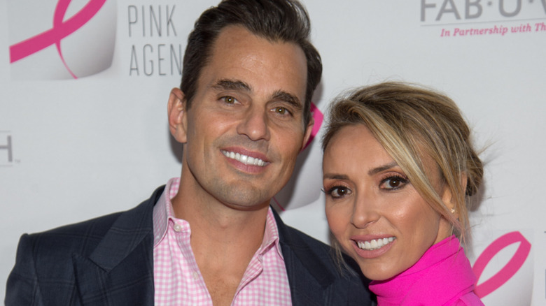 Bill Rancic and Giuliana Rancic, wearing coordinated pink outfits, flash wide smiles.