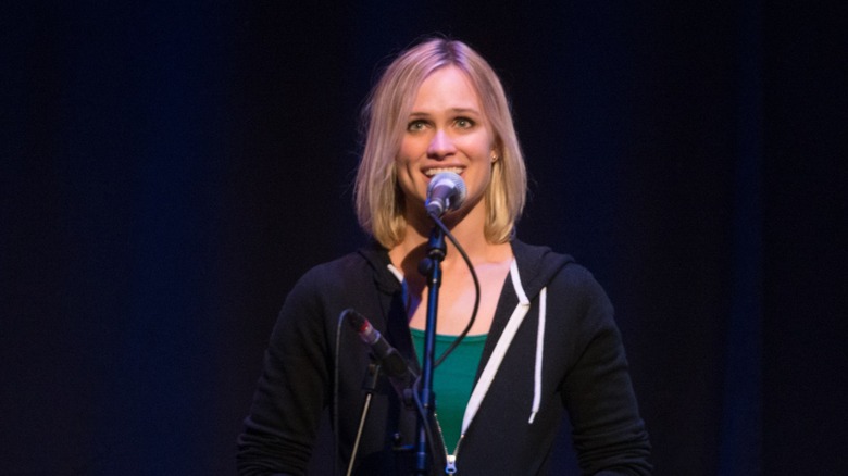 Kelly Kristofferson smiles while singing under the spotlight.