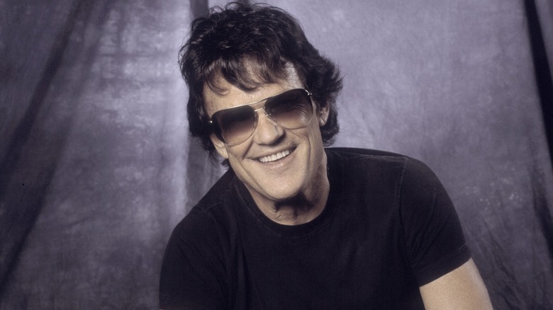 Kris Kristofferson, wearing dark sunglasses, displays a bright smile.