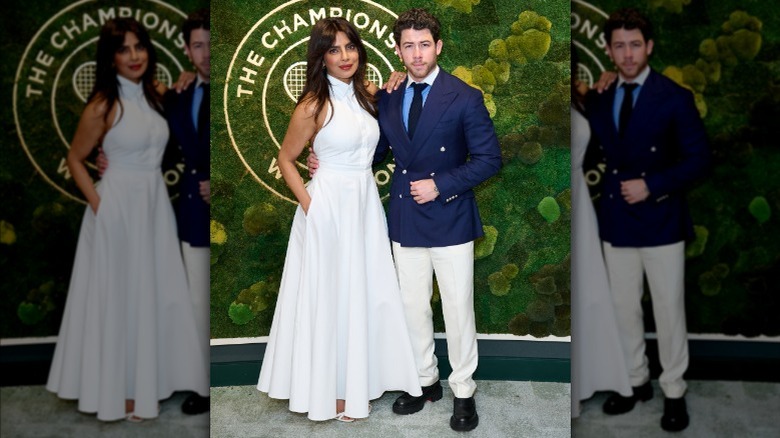 Priyanka Chopra wearing white dress and posing with Nick Jonas, who is wearing a blue blazer, at Wimbledon 2025