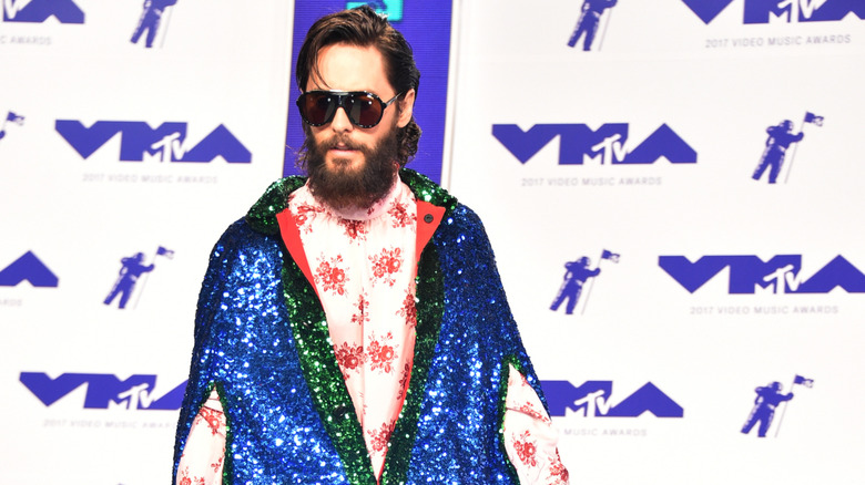 Jared Leto wearing a brightly colored sparkling overcoat and floral undershirt.