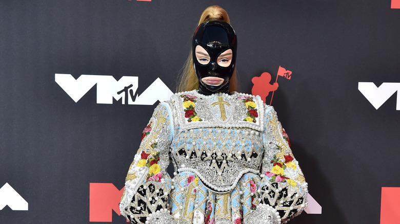 Kim Petras wearing a latex face mask and embroidered and embellished baby doll dress.