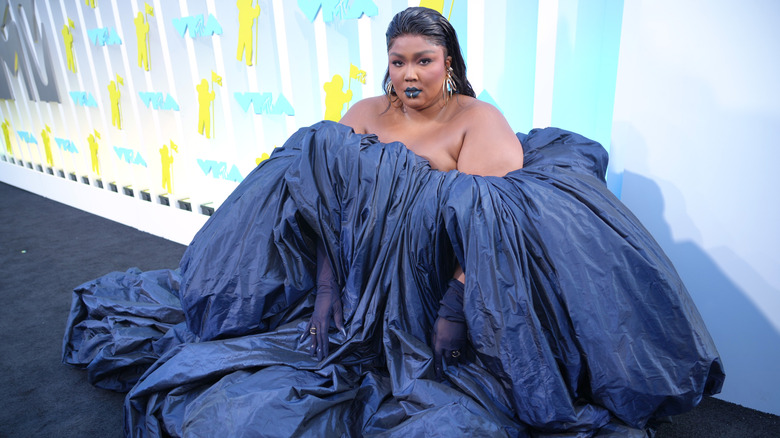 Lizzo wearing a dark blue enormous gown while kneeling on the red carpet.