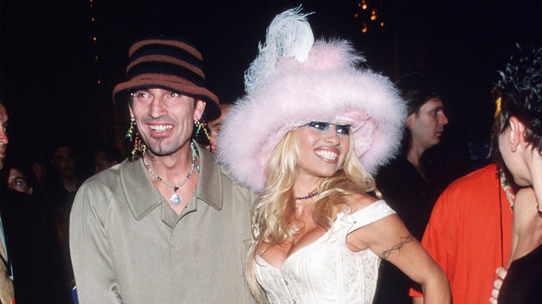 Pamela Anderson wearing a pink fluffy hat and white corset with Tommy Lee wearing a trenchcoat and hat.