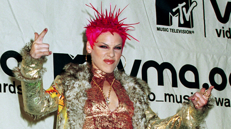Pink sporting pink-spiked hair, a fur coat, and a gold halter crop top.