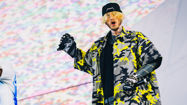 Machine Gun Kelly in yellow and gray camp jacket and backwards hat