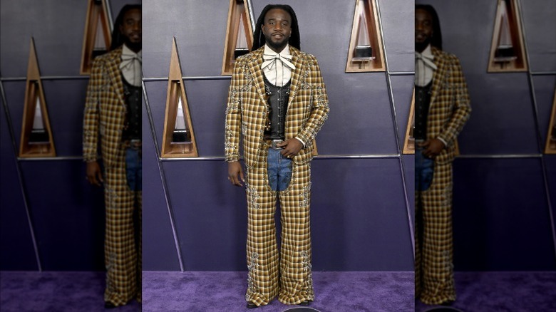 Shaboozey wearing a plaid blazer, chaps, and jeans at the AMAs