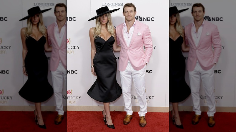 Alix Earle posing in black next to a man in a white and pink suit
