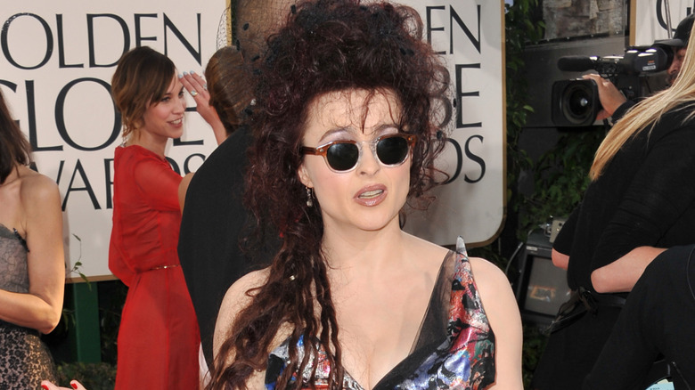 Helena Bonham Carter wearing a colorful asymmetrical gown and sunglasses while holding her arms open