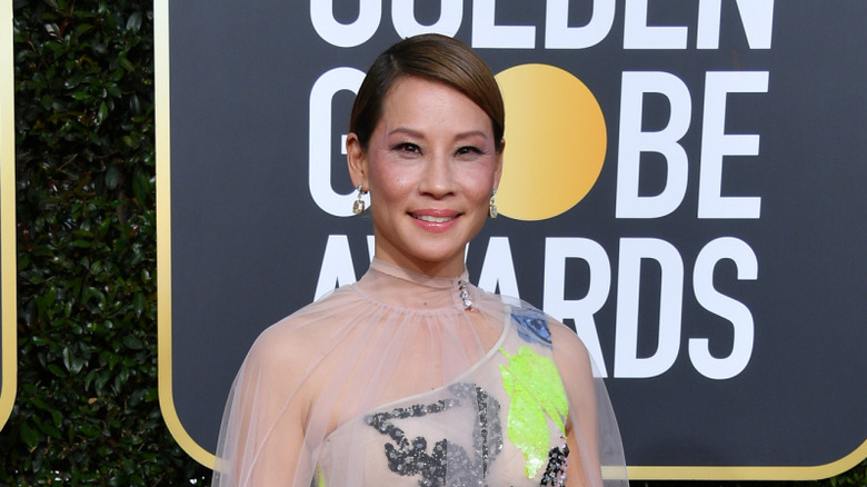 Lucy Liu wearing a sheer gown with colorful beaded patterns sewn into it with a sheer cape laid overtop