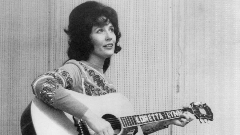 Loretta Lynn plays her guitar with thoughtful expression, 1965