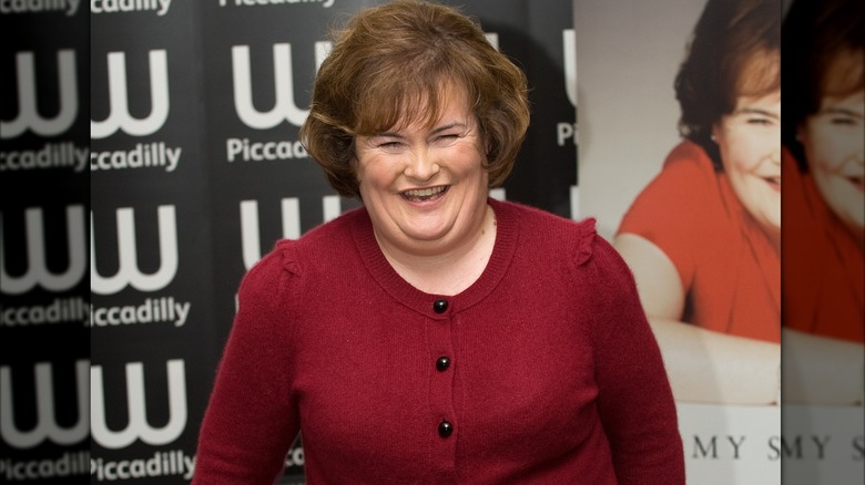 Susan Boyle smiling in a red sweater.
