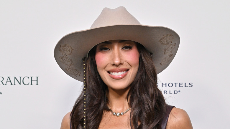 Cheryl Burke, wearing a wide-brimmed hat and wavy hair, is all smiles.