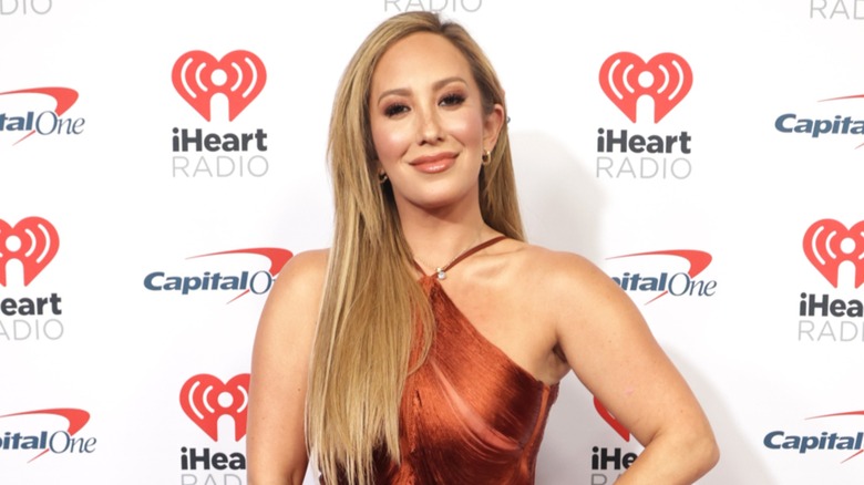 Cheryl Burke smiles softly, with one hand resting on her waist.