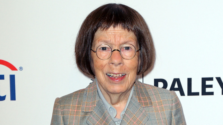 Linda Hunt, wearing a checkered suit, flashes a wide smile.